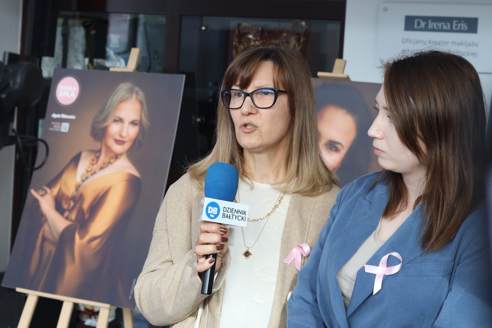 Małgorzata Kozłowska mówi do mikrofonu Dziennika Bałtyckiego, obok stoi Magdalena Raba, w tle portrety z wystawy „KobieTy to siła”