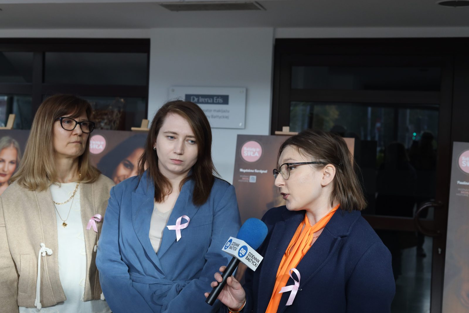 Klaudia Kozak mówi do mikrofonu Dziennika Bałtyckiego, obok stoją Małgorzata Kozłowska i Magdalena Raba, w tle portrety z wystawy